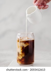 Iced coffee in a tall glass with cream poured over. Cold black coffee with ice cubes in a high glass pour cream. - Shutterstock ID 2055412613