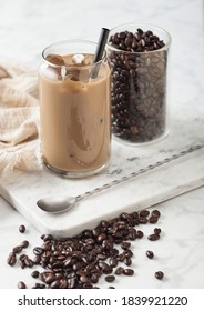 Iced Cold Caramel Coffee With Milk And Glass Container Of Beans And Spoon On Marbel Board And Light Table Background.