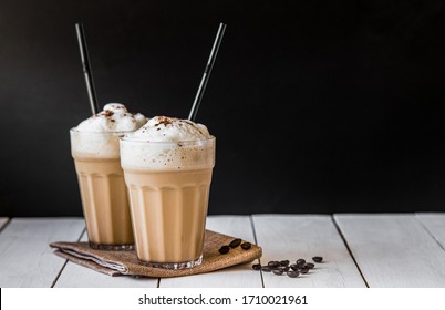 Iced or frappe coffee smoothie on glass cup and Roasted coffee beans on a white table.Black backdrop