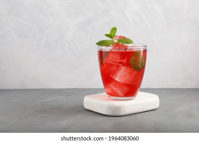 Iced fruit tea or cold watermelon drink in clear glass with mint leaf. Refreshing summer drink. Grey background, copy space. 