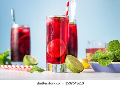 Iced hibiscus tea (karkade, red sorrel, Agua de flor de Jamaica) or lemonade with raspberries, blackberries, mint and citrus on a light grey background. 