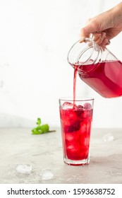 Iced hibiscus tea (karkade, red sorrel, Agua de flor de Jamaica) or lemonade with raspberries and mint on a light grey background. 