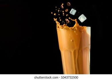 Iced latte coffee splash with ice cubes and roasted beans on a black background