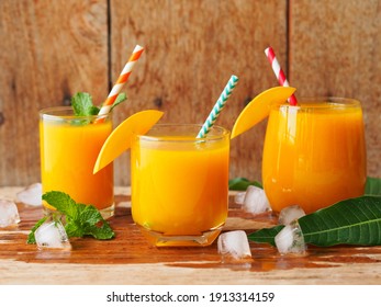 Iced mango juice with fresh ripe mango sliced on a rustic wooden table for summer party drinks concept.