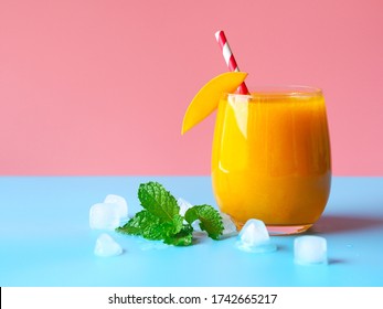 Iced mango smoothies on a pink and blue color background for summer party drinks concept.
