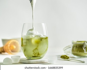 Iced Matcha Latte Tea with pouring whipped cream in tumbler glass. Matcha latte and ingredients on white marble background. Copy space for txt or design - Shutterstock ID 1668835399