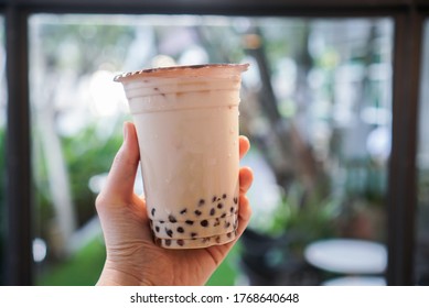 Iced milk bubble tea. Woman holding a plastic cup of milk tea with brown sugar boba/bubble. Center focus. Bokeh background.