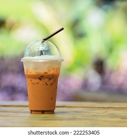 Iced Milk Tea With Straw In Plastic Cup On A Wooden Table In Summer.