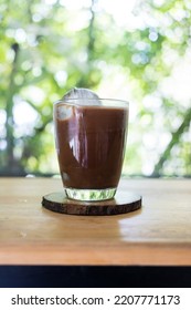 Iced Mocha Coffee In A Transparent Glass On Wooden Saucer With Homemade Ice