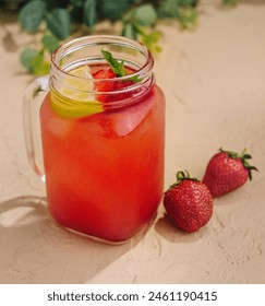 Iced strawberry lemonade garnished with fresh mint and lemon in a mason jar on a sandy background
