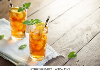 Iced tea with lemon, mint and ice cubes over wooden background, copy space. Iced cold summer drink.