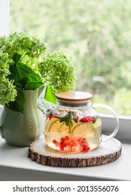 Iced tea with mint, lemon, apple, red currant in a glass teapot and a bouquet of hydrangeas in a ceramic jug on the window in a bright cozy room