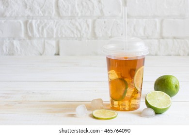 Iced Tea In A Plastic Cup With Straw With Slice Of Lime. White Wooden Plank Background