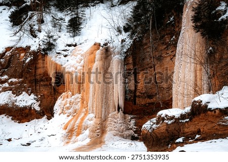 Icefall cascading down a river sandstone cliff on the banks of the Gauja River in winter, revealing natural frozen formations and dramatic geological textures in a tranquil landscape, Springu Rock, Ligatne, Latvia