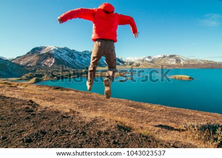 Iceland experiential travel photography, young active man leaping with beautiful snow covered mountains and lake in the background