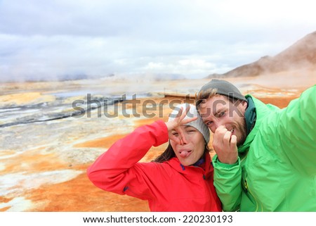 Iceland funny tourists couple having fun taking selfie photo with at landmark destination: Namafjall Hverarondor hverir mudpot also called mud pool hot spring or fumarole. Smell from sulfur on volcano