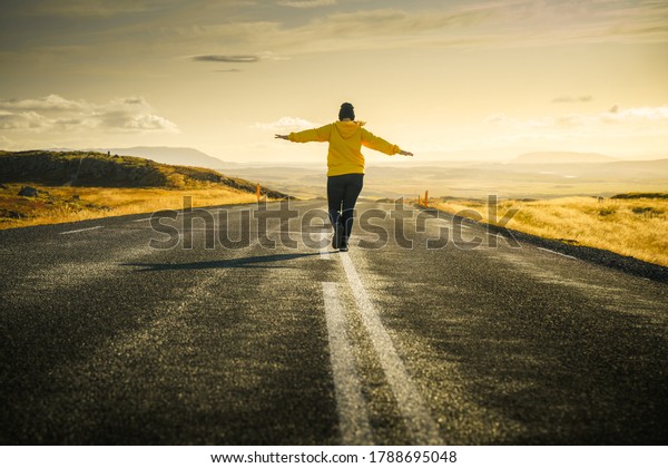 Iceland road trip. Girl is walking\
alone on road to sunset and keeping balance on dividing strip line.\
Freedom concept. Beautiful icelandic\
landscape