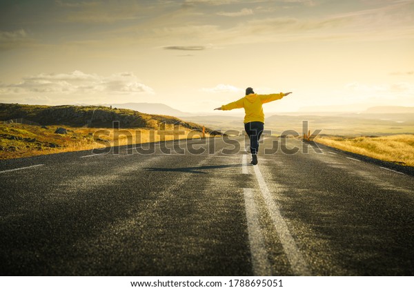 Iceland road trip. Girl is walking\
alone on road to sunset and keeping balance on dividing strip line.\
Freedom concept. Beautiful icelandic\
landscape