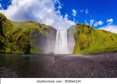  Iceland, Waterfall Skogafoll Summer, Clouds Of Mist. Huge Waterfall Flowing From Under A Giant Glacier