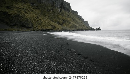 Icelandic black sand beach with rocky cliffs, dark pebbles, and overcast skies, creating a moody, dramatic coastal scene. - Powered by Shutterstock
