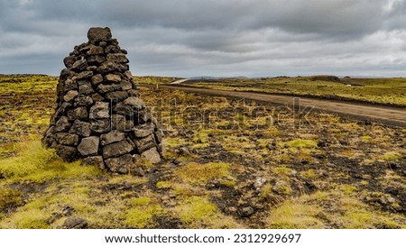 Icelandic colorful and wild landscape with lava field covered by ancient moss with stacked stones as a cairns at dramatic rainy sky, Iceland
