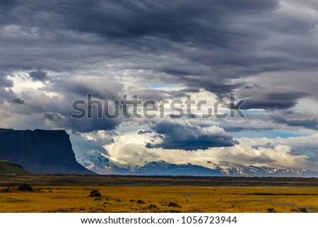 Icelandic rural panorama with grey clouds and snow mountains, near to Kalfafell village, South Iceland