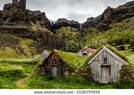 Icelandic turf houses and rocks with waterfall in the background near Kalfafell vilage, Southern Iceland