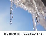 Icicle against light blue sky. Drop of melted snow falls down. Closeup. Illustration about end of winter or beginning of spring. Thaw. Macro