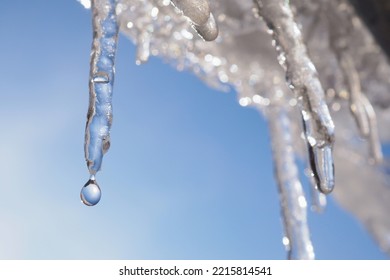 Icicle against light blue sky. Drop of melted snow falls down. Closeup. Illustration about end of winter or beginning of spring. Thaw. Macro