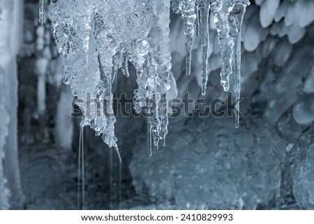 Icicles with clear water drops at a creek cascade waterfall on a very cold winters day in Sauerland Germany. Close up macro of transparent and translucent turquoise blue shapes with blurred background