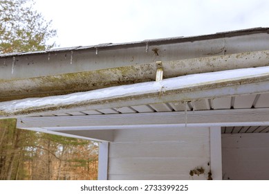 Icicles hang off broken gutter of after recent snowstorm scene shows winter weather conditions.
