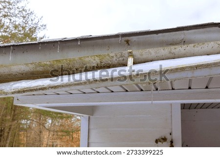 Icicles hang off broken gutter of after recent snowstorm scene shows winter weather conditions.
