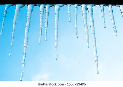 Icicles hang on the roof of a house against a bright blue sky. Spring landscape with icicles hanging from the roof of the house. Set of snow icicles, snow hat.