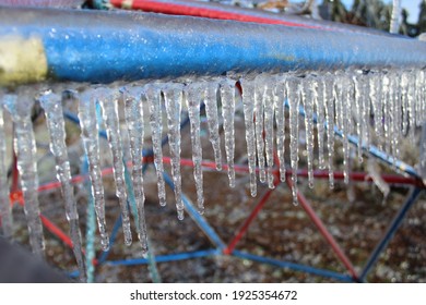 Icicles Hanging From The Blue Metal Bar Of A Child’s Climbing Dome. Freezing Rain On A Playground. Dangerous Equipment