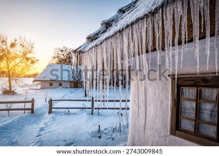 Icicles are hanging on thached straw roof of old village house at beautiful winter sunset