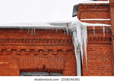 Icicles on gutter and roof. Huge Icicles hanging down from drain pipe of the red building. Icy facade of building, dangerous icicles melt on rooftop, risk of injury. Ice hazard - Powered by Shutterstock