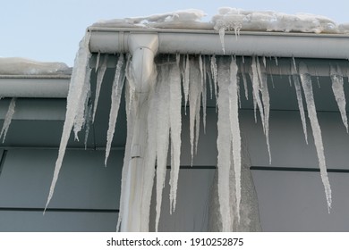 Icicles on the roof. The drain is full of snow and ice. Icicles falling danger concept.