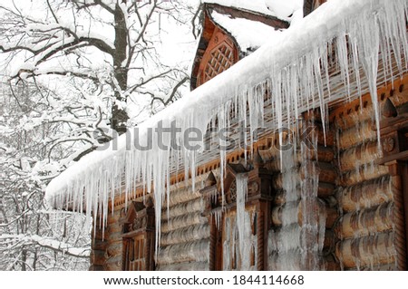 Icicles in winter. The old hut is covered with ice in winter. Icicles hang from the roof. The wooden tower is covered with ice. Icicles hang on the roof of a house. The logs of the hut were frozen