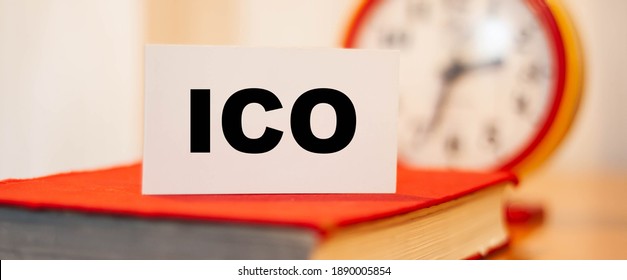 ICO Business Clause On A Closed Book And Orange Clock.