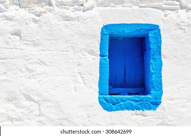 Iconic blue wooden window on white stone wall of typical Greek house, Greece