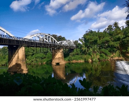 An iconic bridge across Manimala river, Kerala on a pleasant sunny day. Vehicles passing the bridge and water flowing beneath. A reflection of river is also visible in the water
