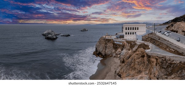 The iconic Cliff House sits on a cliff in San Francisco, California, with rocky outcrops in the Pacific Ocean and a winding road nearby under an overcast sky. - Powered by Shutterstock