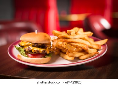 Iconic Diner Double Cheeseburger Of Stacked Juicy Beef Patty And Melted Cheese On Lettuce And Tomato Between Soft Potato Buns With Thick Steak Cut Golden French Fries And Red Booth Blurry Background