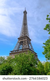 Iconic Eiffel Tower structure against a bright blue sky with fluffy clouds and green foliage