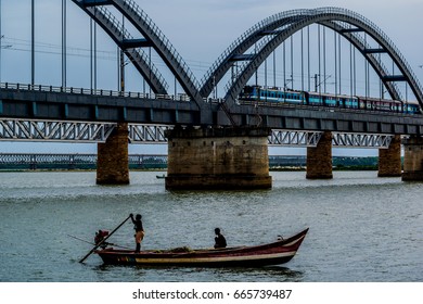 The iconic Godavari arch bridge with a train passing through it and a fishing boat with fishermen down below in the godavari river in the rajahmundry city.