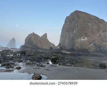 Iconic Haystack Rock and dramatic sea stacks at Cannon Beach, Oregon, at low tide during dusk.