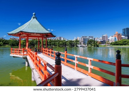 Iconic hexagonal red pavilion landmark from Ohori lake park with Fukuoka city view against blue sky, Kyushu, Japan. Famous travel destination in autumn or fall season.