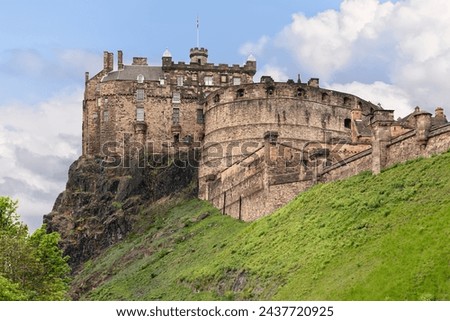 An iconic image of Edinburgh Castle, with its historic battlements and robust stonework, overlooking the city from its perch on Castle Rock, under a canopy of white clouds and blue sky