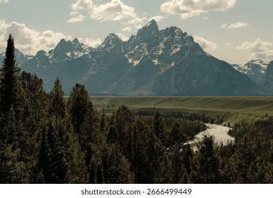 The iconic, panoramic view from Snake River Overlook in Grand Teton National Park. A pine forest leads to the curving river below the majestic, snow-capped Teton mountain range.