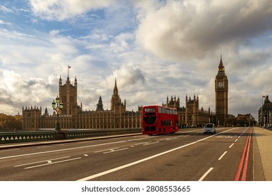An iconic red double-decker bus drives across Westminster Bridge in London. In the background stands the Palace of Westminster with the Big Ben clock tower under a bright sky filled with large white and dramatic grey clouds scene.